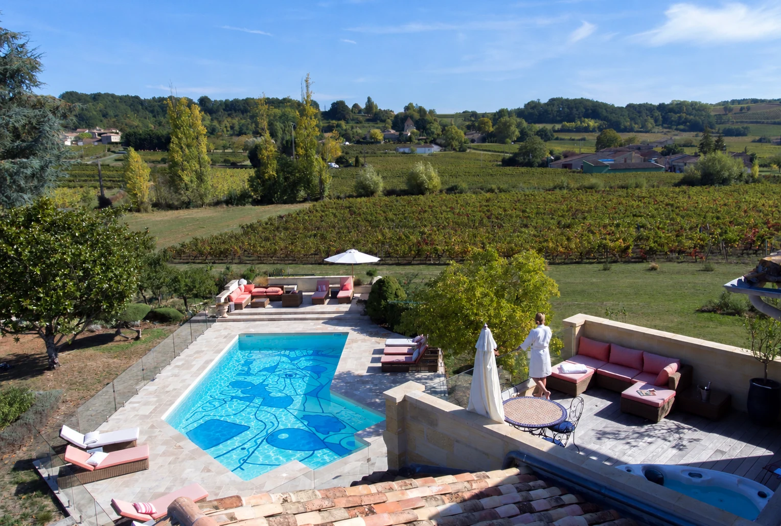 Terrasse avec une femme face à la piscine au fond artistique et aux vignes